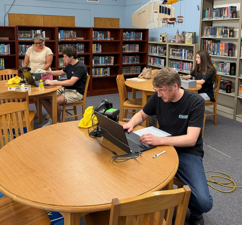 Technicians fingerprinting staff at laptop scanning stations set up in a school library